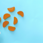 Orange gummy supplements spilling from a white bottle, illustrating excipient selection in gummy formulation