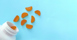 Orange gummy supplements spilling from a white bottle, illustrating excipient selection in gummy formulation