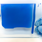 Paint quality testing in a coatings laboratory with a blue coating sample being evaluated on a glass panel.
