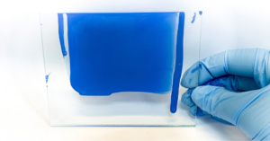 Paint quality testing in a coatings laboratory with a blue coating sample being evaluated on a glass panel.