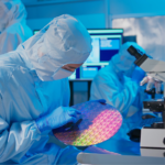 Cleanroom technician inspecting a silicon wafer beside a microscope and monitoring equipment