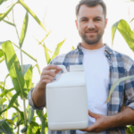 Farmer smiling and holding a white pesticide bottle in a corn field, ensuring crop protection and healthy growth.
